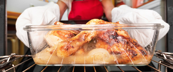 Panorama of woman taking roasted chicken from the oven. Cooking in the oven . 