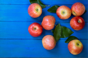 Red and pink apples with  green leaves on blue wooden table , close up from above , copy space