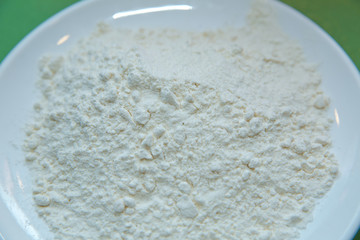 Flour in the plate green background . Close-up heap with wheat flour coarse in white plate on green background. Left on the photo . Portion of Milk Powder close-up shot on green background