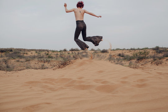 Unrecognizable topless redhead girl making sand splashes in desert