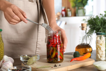 Woman taking pickled chili pepper from jar at wooden table indoors, closeup