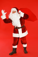 Authentic Santa Claus with bag full of gifts on red background