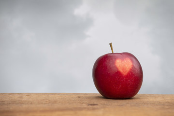 Apple with a heart shape on skin sits on a wooden surface outside