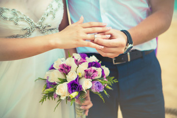 Obraz na płótnie Canvas Hands and rings on wedding bouquet on the beach