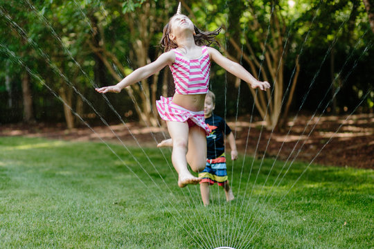 Young girl jumping through a water sprinkler