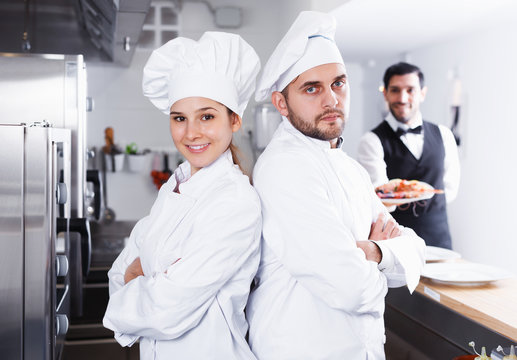 two chefs, standing back to back in kitchen
