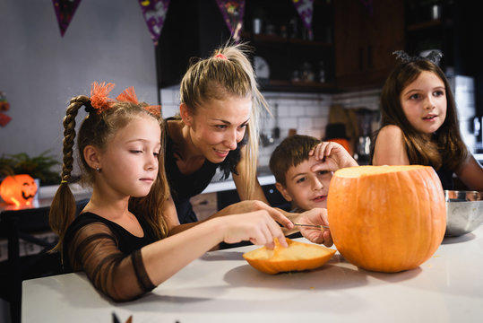 Mother carving Halloween pumpkin with children at decorated home kitchen
