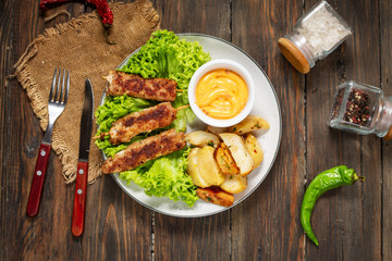 Grilled shish kebab served with fried potatoes and sauce on wooden background
