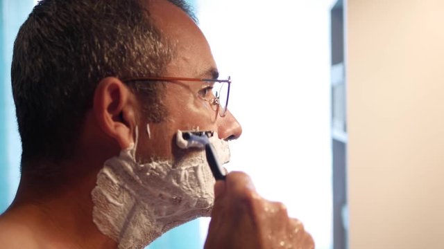 Man shaving with foam and manual razer. Close up of man shaving beard