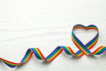 LGBT rainbow ribbon in the shape of heart. Pride tape symbol. White wood background. Copy space for text.