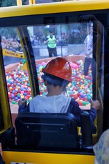 Young boy operating a mini excavator toy digging for colorful  plastic balls out of a kiddy pool while wearing a hard hat