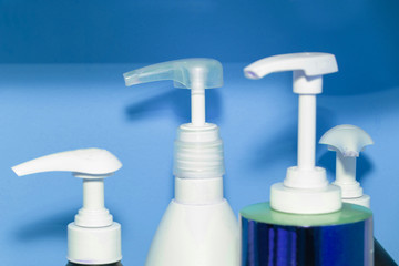 Three bottles of shampoo or shower gel, cream dispenser on colored background with copy space.