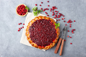 Homemade flavored pie with fresh cowberry or lingonberry on a gray stone background with branches of northern wild cowberry.
