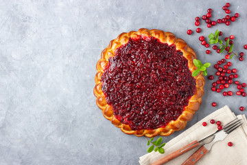 Homemade flavored pie with fresh cowberry or lingonberry on a gray stone background with branches of northern wild cowberry.