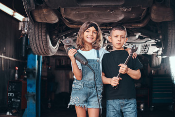 Smiling girl and pensive boy are posing for photographer at auto service workshop.