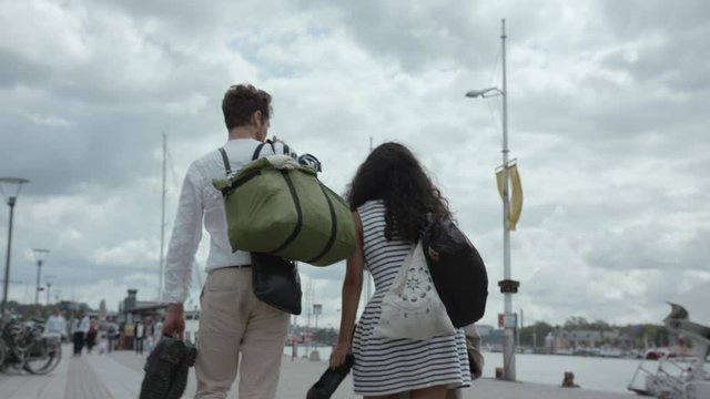 A young travelling couple walking barefoot, shoes in hand, in the harbour.