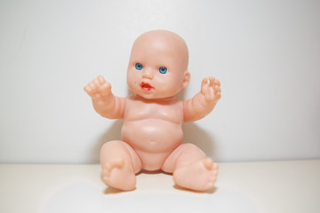 Cute little naked baby doll with blue eyes sitting or walking . Copy space.There is no clothes on the doll . baby doll isolated in white background closeup . Doll white background no clothes .