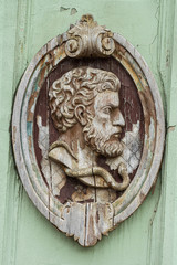Wooden sculpture of male head in elliptical decorative frame, old and weathered, decorative relief on an old building