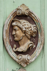 Wooden sculpture of female head in elliptical decorative frame, old and weathered, decorative relief on an old building