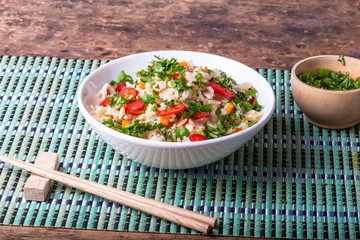Fried rice with egg, ham and vegetables in a bowl on a bamboo napkin, chopsticks