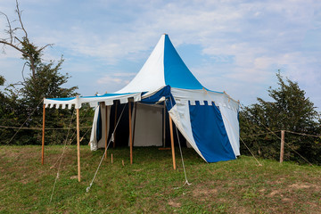 Blue and white medieval tent standing on the hill top with blue sky and white clouds in the background