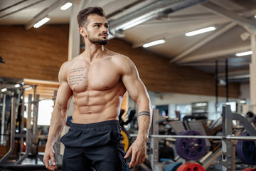 Attractive muscular athletic young man bodybuilder fitness model posing after exercises in gym.