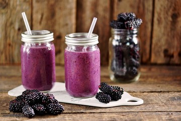 Obraz na płótnie Canvas Healthy blackberry organic smoothie with natural yogurt and honey in a glass jar on an old wooden background.