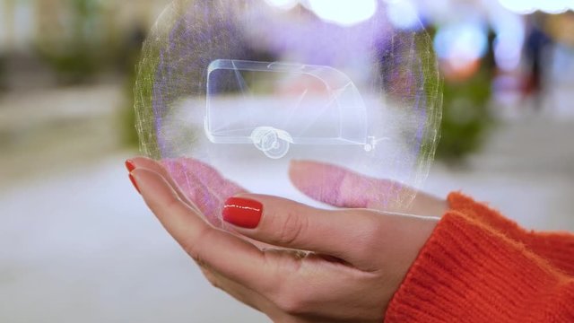 Female hands holding a conceptual hologram with Trailer house. Woman with red nails and sweater with future holographic technology on a blurred background of the street