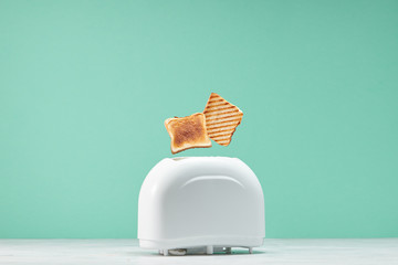 Roasted toast bread popping up of toaster with green wall, front view - obrazy, fototapety, plakaty