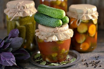 Different pickled cucumbers - whole and slices with onions, carrots in tomato juice on an old wooden background.