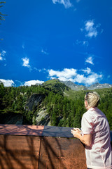 Frau blickt zu Schutzhütte über Schlucht hinweg vor blauem Himmel mit Wolken und grünen Wald im...