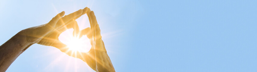 Hände von Mädchen / Frau bilden ein Herz aus ihren Fingern - Hintergrund blauer Himmel mit Sonne