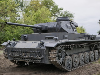 Fototapeta na wymiar German medium tank of the Second World war in working order. the tank is painted black against a background of green trees in summer .