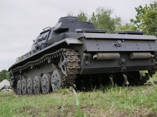 German medium tank of the Second World war in working order. the tank is painted black against a background of green trees in summer .