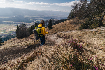 Obraz premium A hiker walking on a mountain meadow in spring or autumn. Burnt out yellow grass, cloudy day. Hiking in the mountains of Slovenia. Alpine mountain landscape and trekking in it.