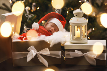 Cute newborn baby wearing Santa Claus hat is sleeping in the Christmas gift box