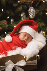 Fototapeta na wymiar Cute newborn baby wearing Santa Claus hat is sleeping in the Christmas gift box