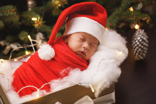 Cute newborn baby wearing Santa Claus hat is sleeping in the Christmas gift box