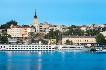 Blue hour view of Belgrade riverfront with Sava river in the foreground, holy archangel Michael cathedral at the back and impressive, large cruiser ship in the harbor
