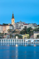 Blue hour view of Belgrade riverfront with Sava river in the foreground, holy archangel Michael cathedral at the back and impressive, large cruiser ship in the harbor