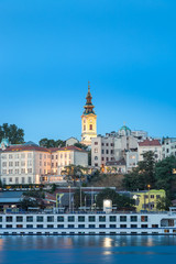 Blue hour view of Belgrade riverfront with Sava river in the foreground, holy archangel Michael cathedral at the back and impressive, large cruiser ship in the harbor