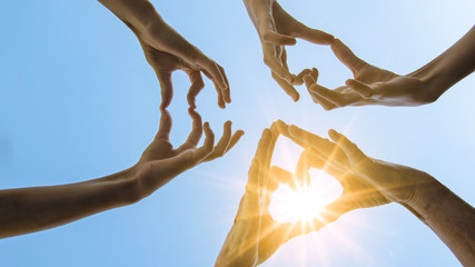 Hände von Mädchen / Frau bilden ein Herz aus ihren Fingern - Hintergrund blauer Himmel mit Sonne