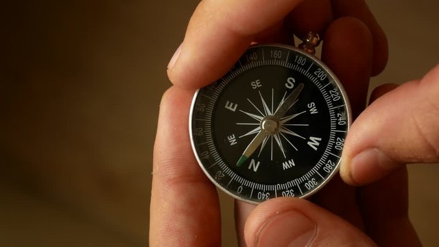 Male hands hold the compass and set needle to the north. Checking direction with a compass in hands. Close up shot of a spinning vintage compass.