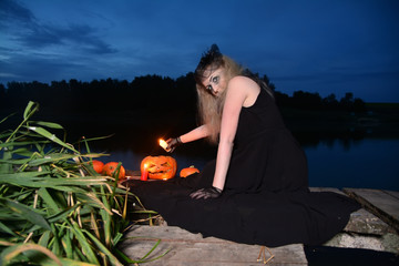 Witch with a candle and a pumpkin near the magic swamp in Halloween. Beautiful young woman near the reeds in a mystical setting.