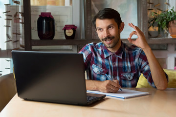 Fototapeta premium A man working on the Internet writes in a notebook and makes hand gestures