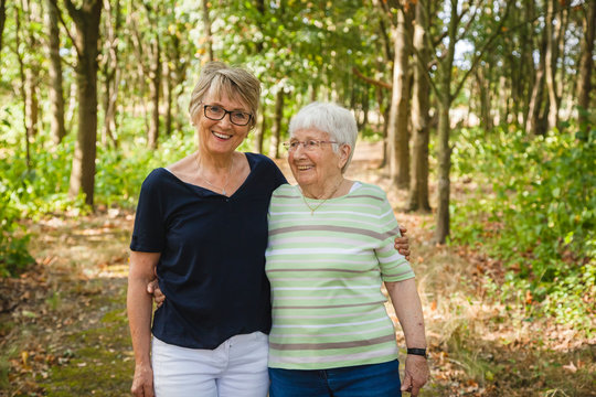 Senior lady with her aged mother with dementia, embracing and smiling in a summer park