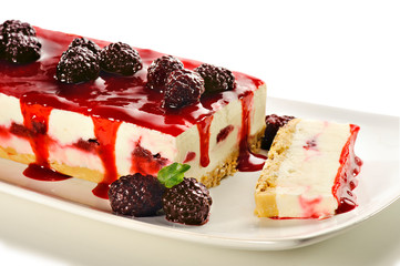 Cheesecake with raspberry jam as topping and raspberries decorating, on a white ceramic plate. For a holiday celebration or party.