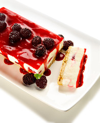 Cheesecake with raspberry jam as topping and raspberries decorating, on a white ceramic plate. For a holiday celebration or party.