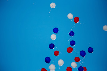 Red, white, blue helium balloons are flying into the blue sky