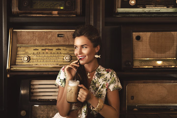 Young happy woman drinking iced coffee in stylish retro cafe